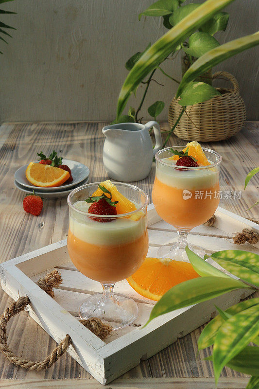two orange puddings in glasses garnished with sliced ​​oranges and strawberries